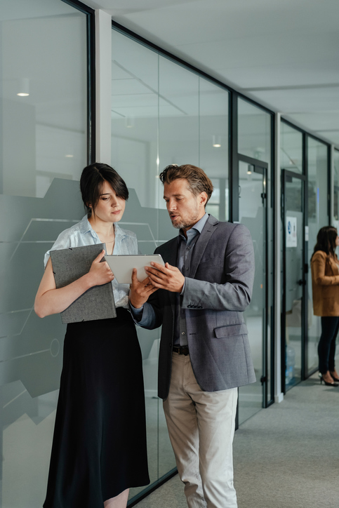 Serious Businessman and Businesswoman Working Together on a Digital Tablet in a Office Hallway