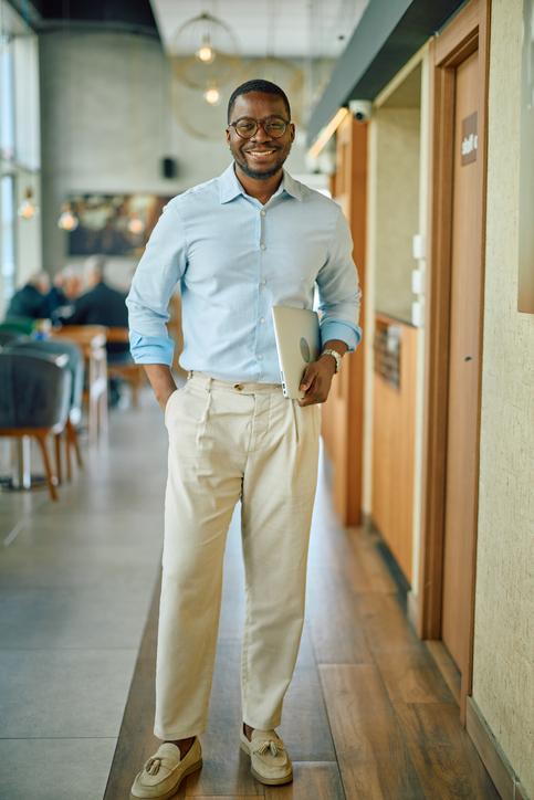 Smiling african american businessman walking in office corridor holding laptop